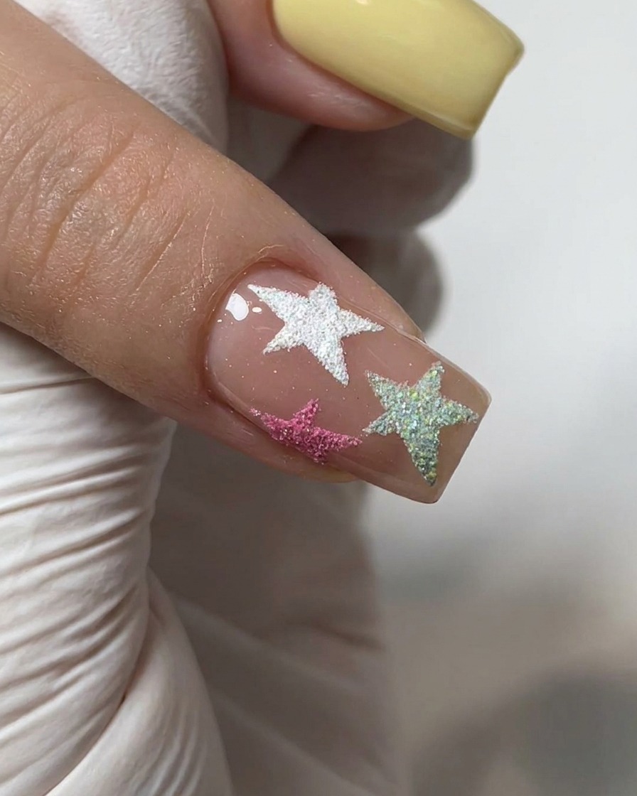 Ein Pinsel trägt einen klaren Glanz-Top-Coat über einen Nagel auf, der mit Chrompulver und strukturierten Sternen dekoriert ist.