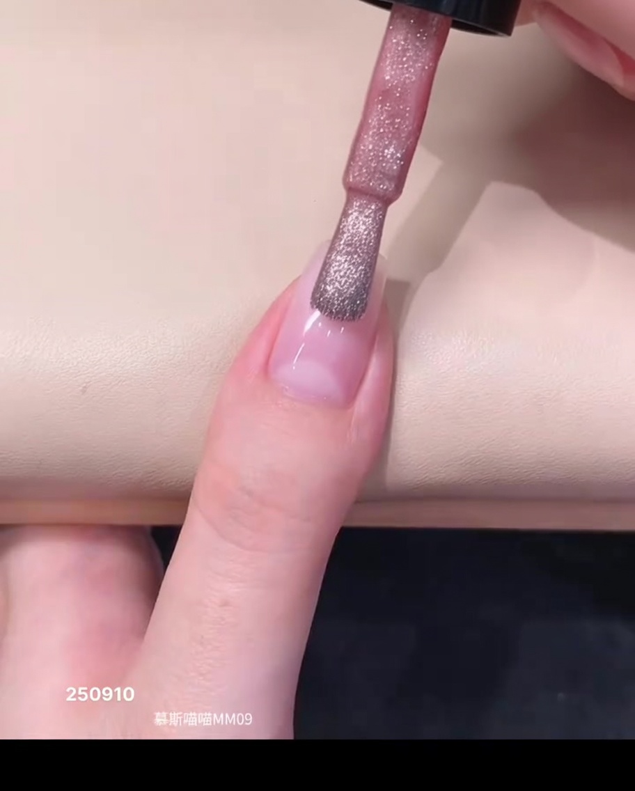 Ein Fläschchenpinsel trägt einen Tropfen zartrosa Magnet-Gelack im Nagelhautbereich eines Naturnagels auf.