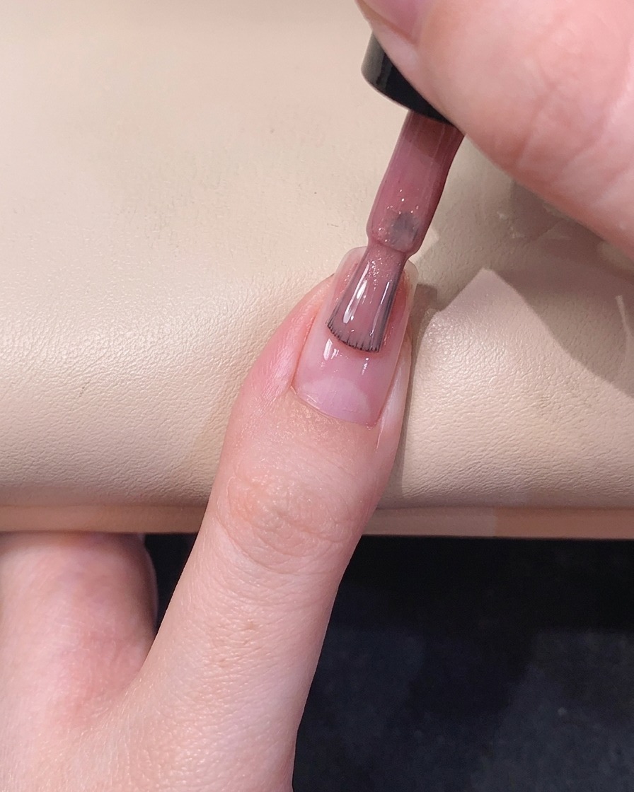 Ein Gel-Pinsel gleitet die Mitte des Fingernagels hinab und verteilt einen zartrosa, glitzernden Lack.