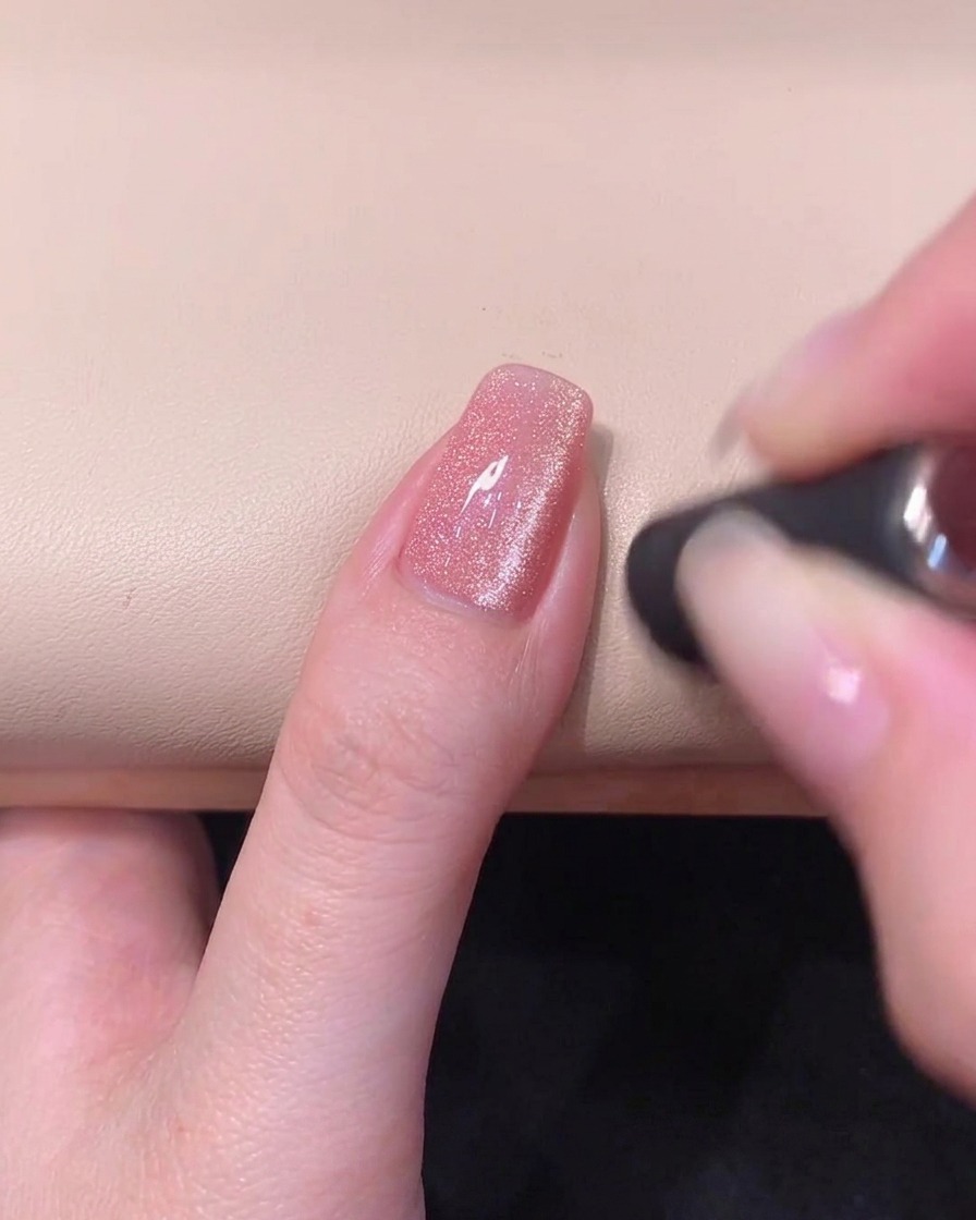 Ein Zylindermagnet wird waagerecht über die vordere Nagelspitze gehalten, um ein helles Cat-Eye-Band zu formen.