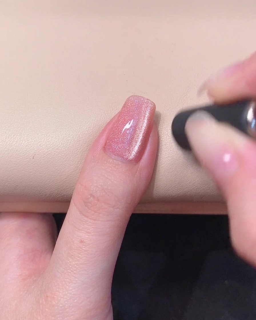 Eine Nahaufnahme eines rosa Gel-Nagels mit einem leuchtenden magnetischen Cat-Eye-Streifen in der nassen Geloberfläche.