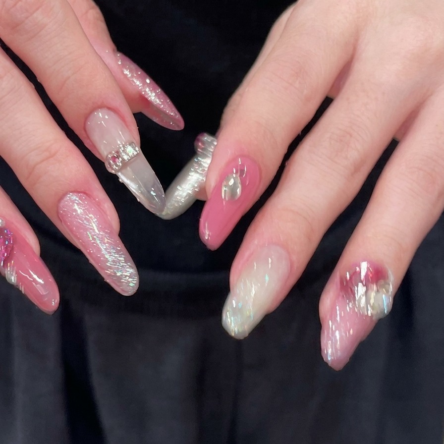 Eine Nahaufnahme von Händen mit gespreizten Fingern, die vollständig dekorierte rosa und silberne lange Mandelnägel mit glitzernden Strass-Akzenten enthüllen.