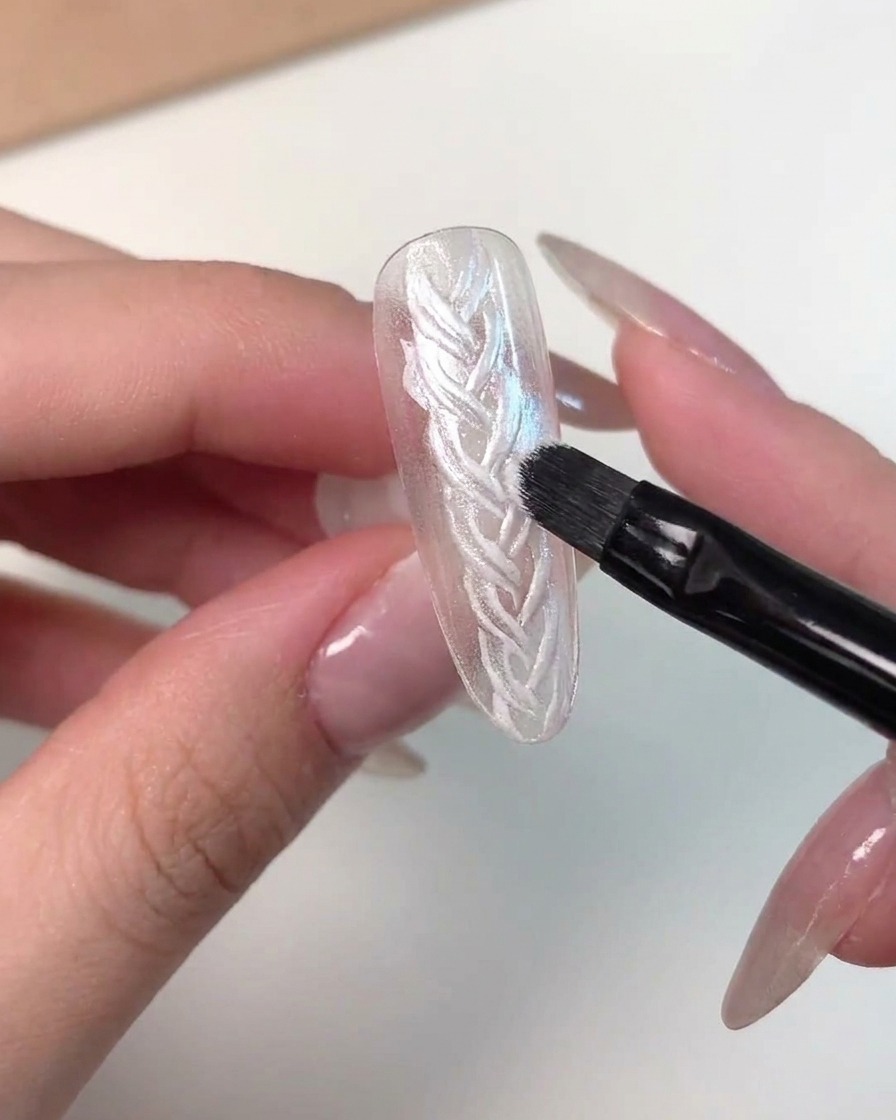 Eine detaillierte Nahaufnahme zeigt, wie ein Pinsel rosa magnetisches Cat-Eye-Gel auf eine Nagelspitze aufträgt.
