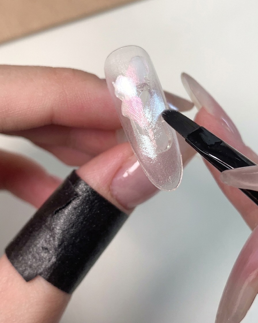 Eine Nahaufnahme zeigt, wie blaues Gel um die äußeren Ränder des Nagels aufgetragen wird.