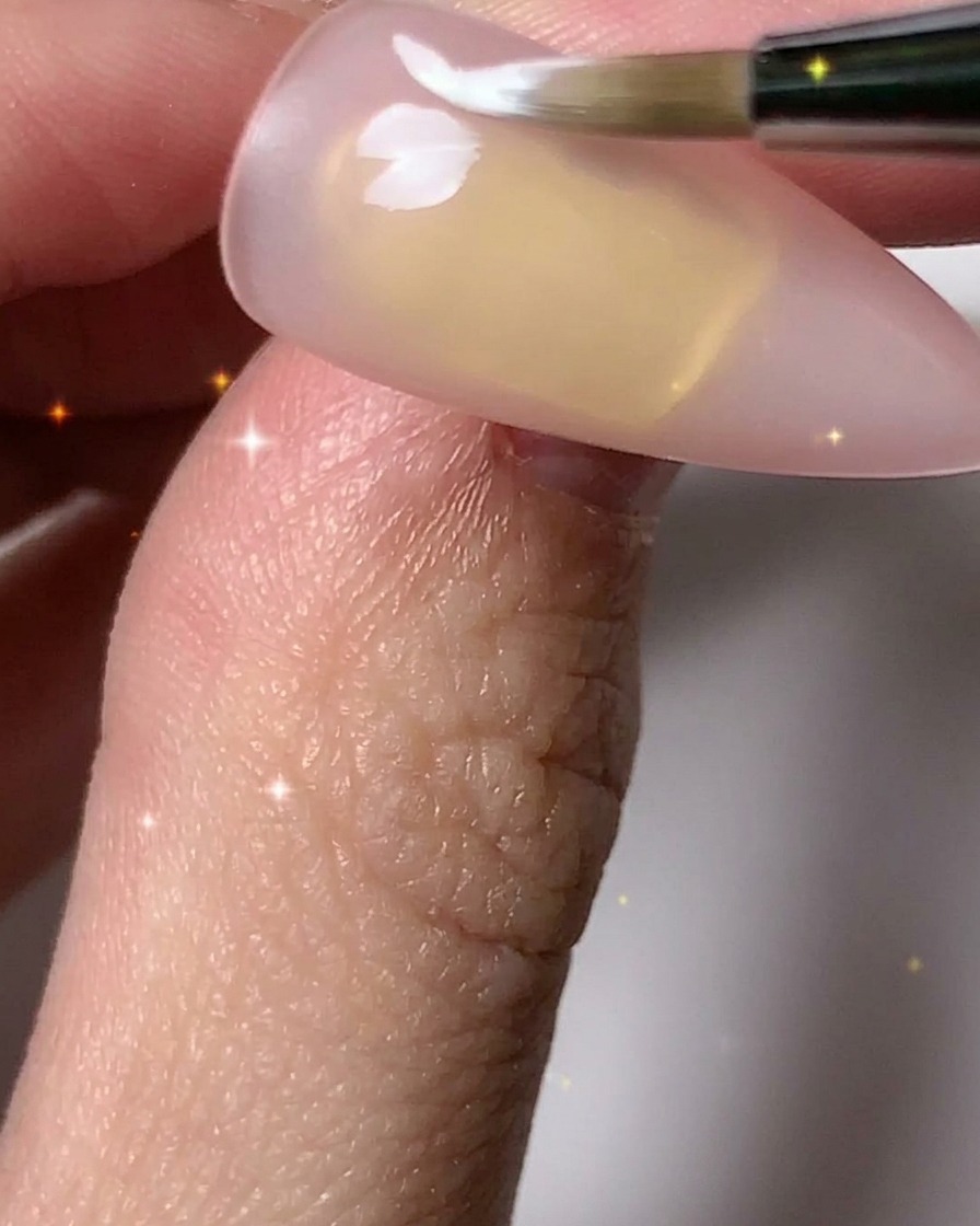 Ein Nagelpinsel fügt weiße Blütenblätter hinzu, um mehrere Blumenkonturen auf der Nagelplatte zu vervollständigen.