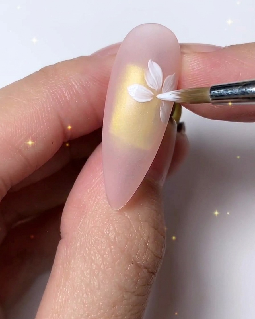Ein feiner Pinsel verfeinert und schichtet weiße Blütenblätter für einen zarten Look auf dem Nagel.