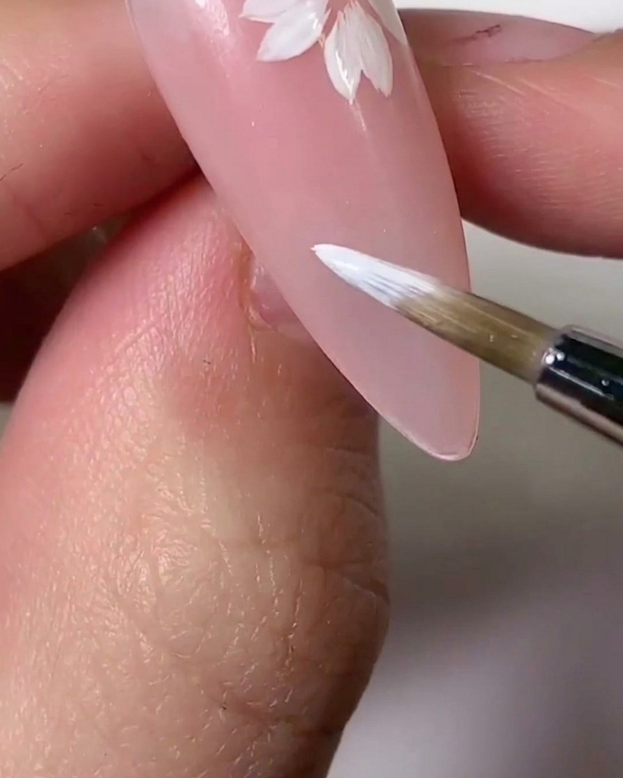 Ein Pinsel trägt eine hellrosa Gel-Tönung über Teile der weißen Blütenblätter auf, um einen Verlaufseffekt zu erzielen.