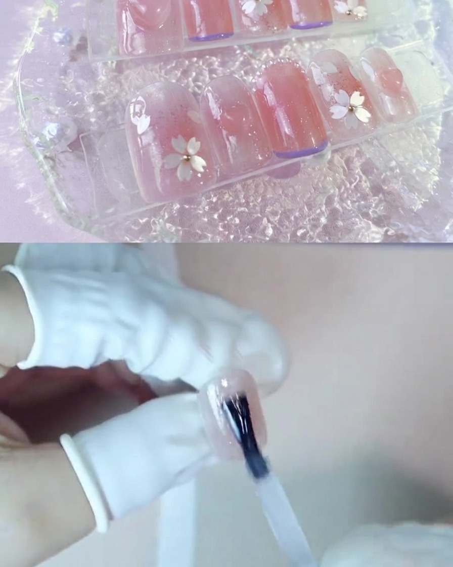 Eine Hand trägt eine Schicht klares Verstärkungsgel über einem rosafarbenen Blush-Nagel auf.