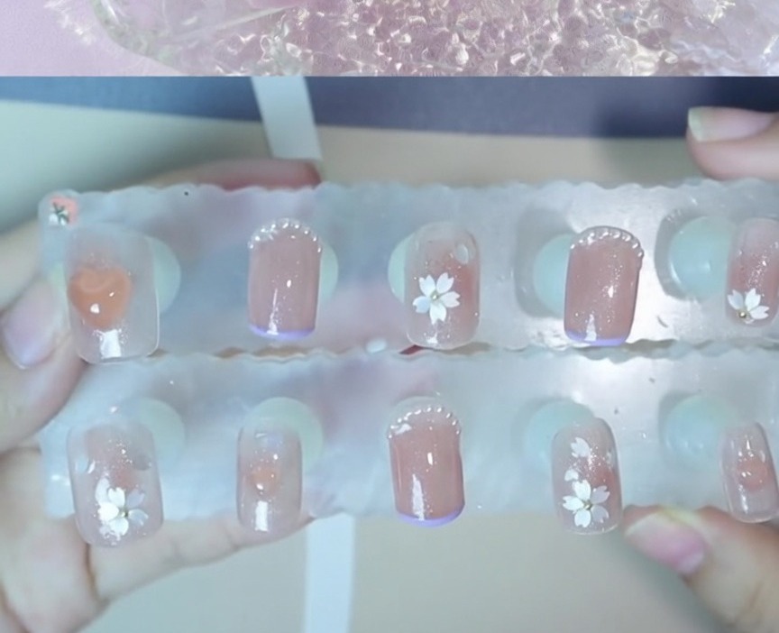 Eine Nahaufnahme einer kleinen Stahlperle, die in der Mitte eines floralen Nageldesigns positioniert wird.