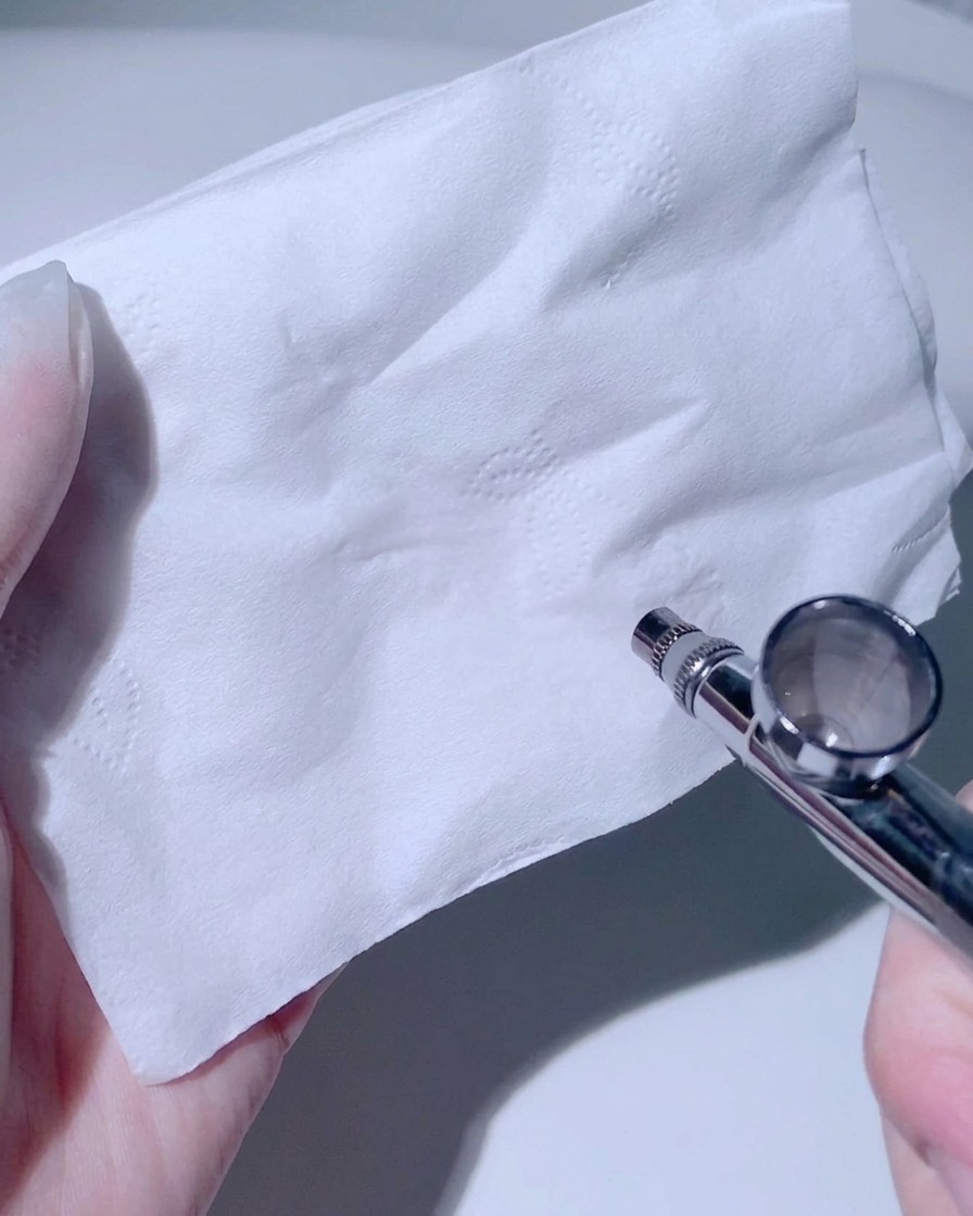 Eine Airbrush-Düse zeigt auf ein weißes Papiertaschentuch und testet den Sprühstrahl.