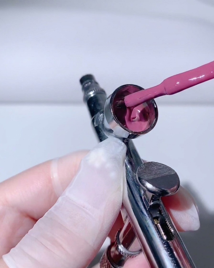 Ein Pinselapplikator gießt pinkfarbenes Gel an der inneren Seitenwand eines Airbrush-Bechers herunter.