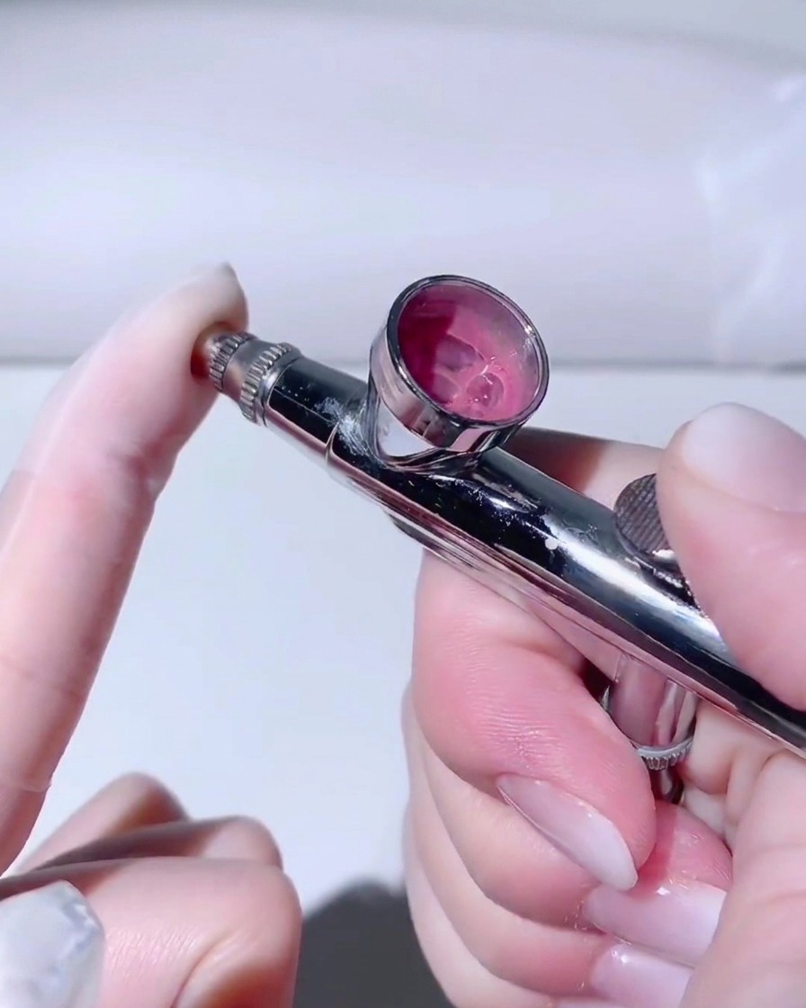 Ein behandschuhter Finger bedeckt die Airbrush-Düse, während die andere Hand den Auslöser drückt.