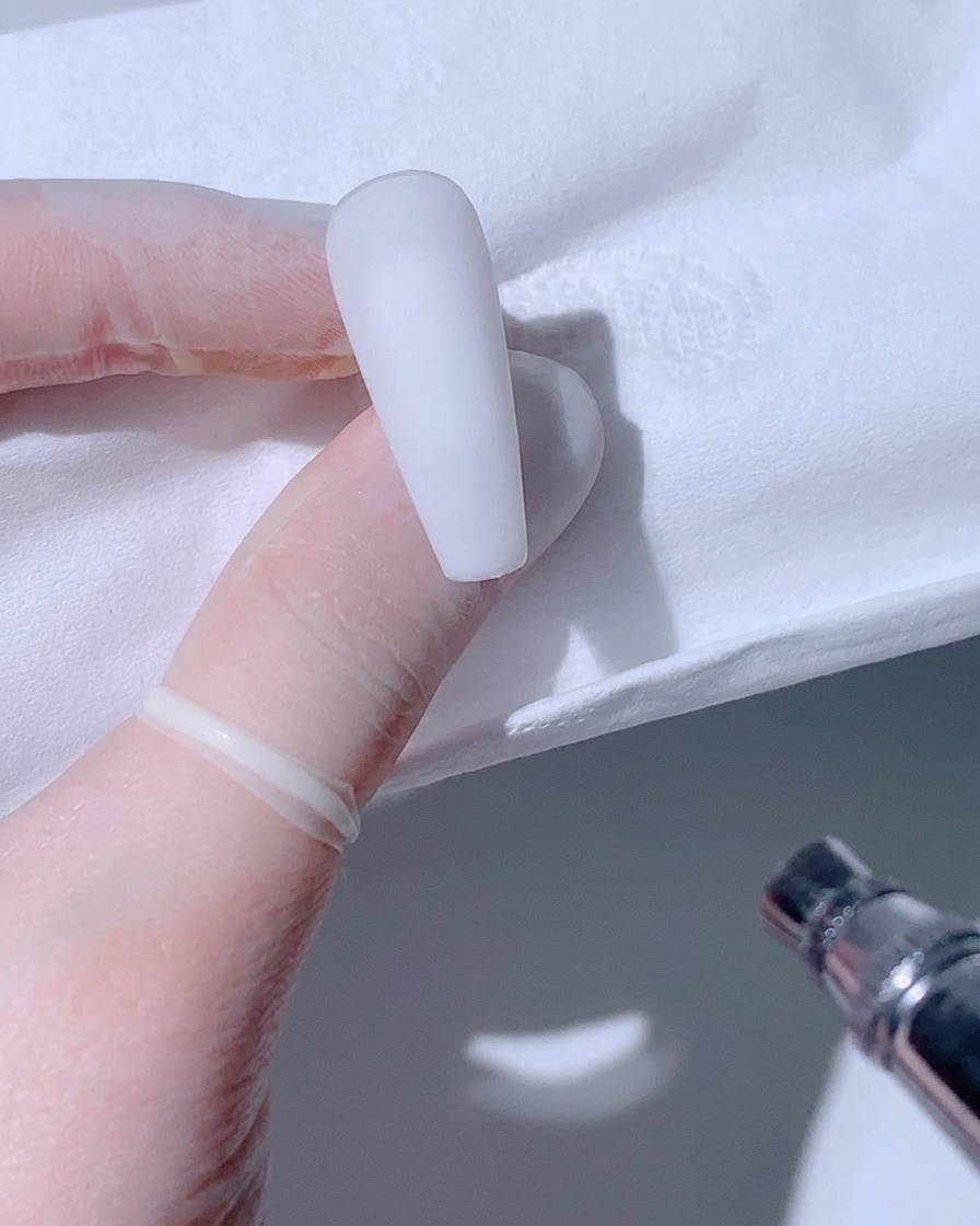 Nahaufnahme einer matten weißen Nagelspitze in behandschuhten Händen, bereit für die Airbrush.