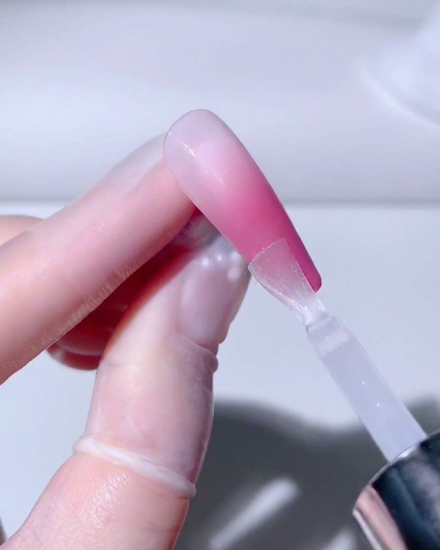 Ein Pinsel trägt eine klare, glänzende Schicht Versiegelungsgel auf den fertigen Ombré-Nagel auf.