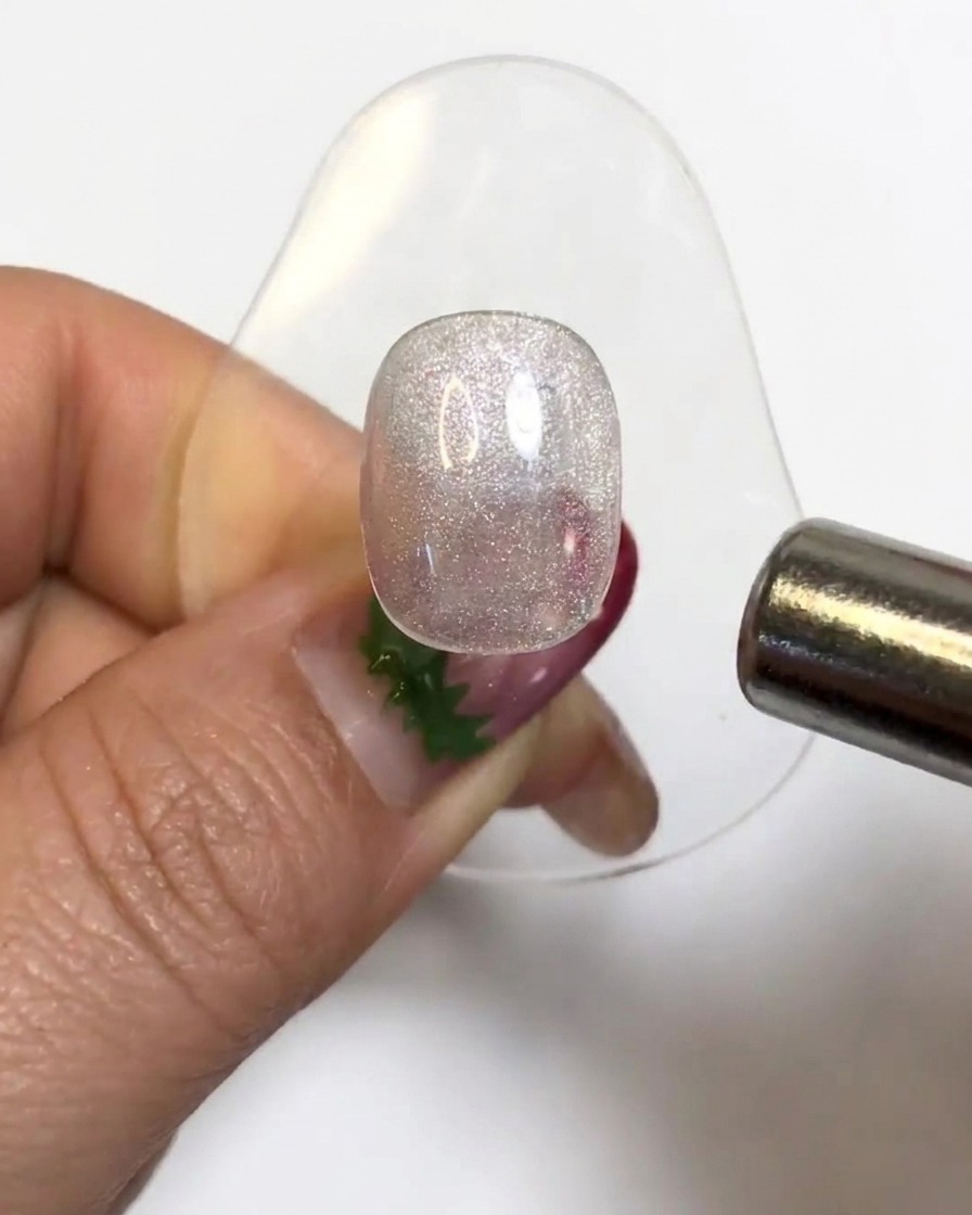 Ein zylindrischer Magnet schwebt über einer glitzernden Gel-Nagelspitze, um die Cat-Eye-Partikel zu aktivieren.