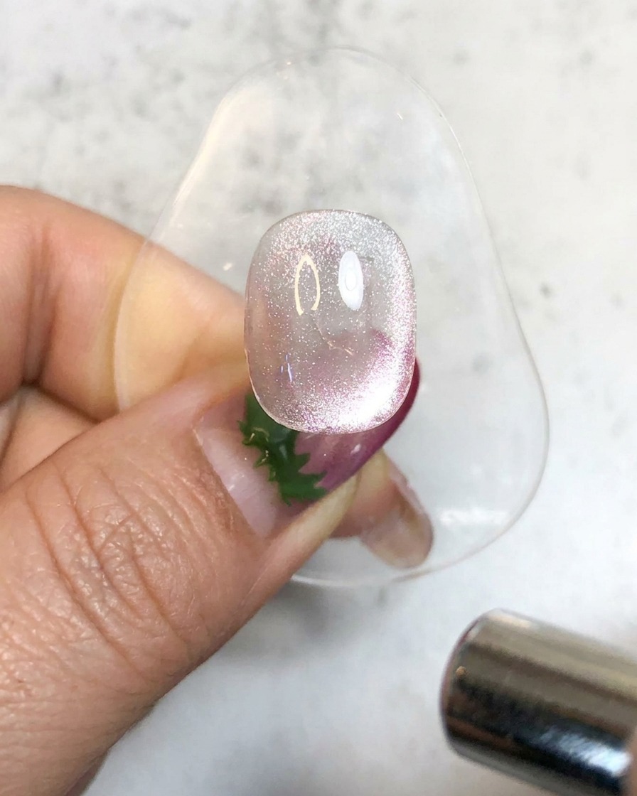 Eine Hand-UV-Lampe beleuchtet einen glitzernden magnetischen Gel-Nagel auf einem Ständer zum Aushärten.