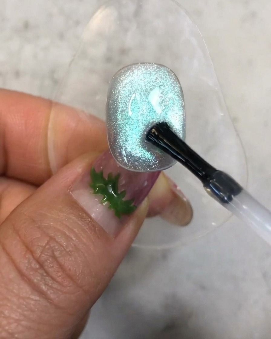 Ein Pinsel trägt einen kleinen Tropfen klarem Aufbau-Gel auf die strukturierte blaue Cat-Eye-Nageloberfläche auf.