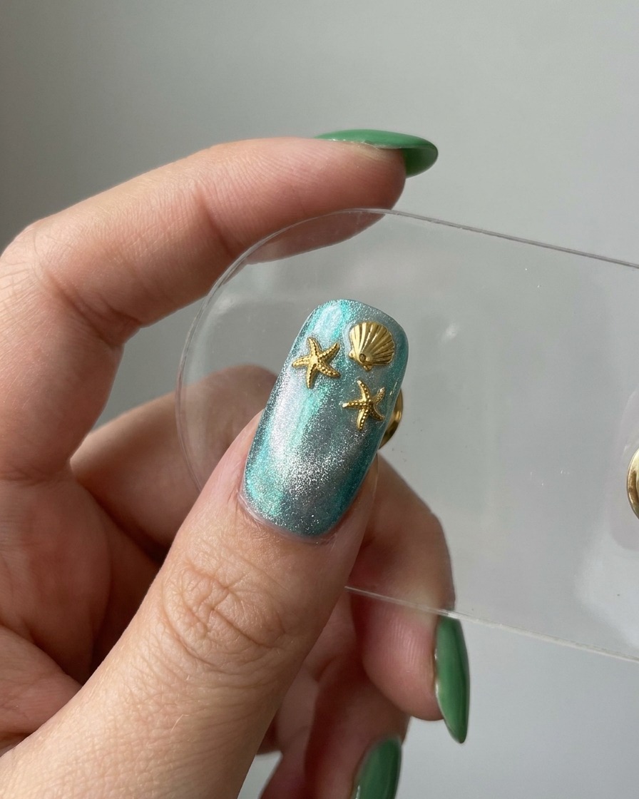 Eine Vorschau des fertigen Nagels zeigt eine blaue Cat-Eye-Basis, die mit Goldseestern- und Muschel-Charms dekoriert ist.