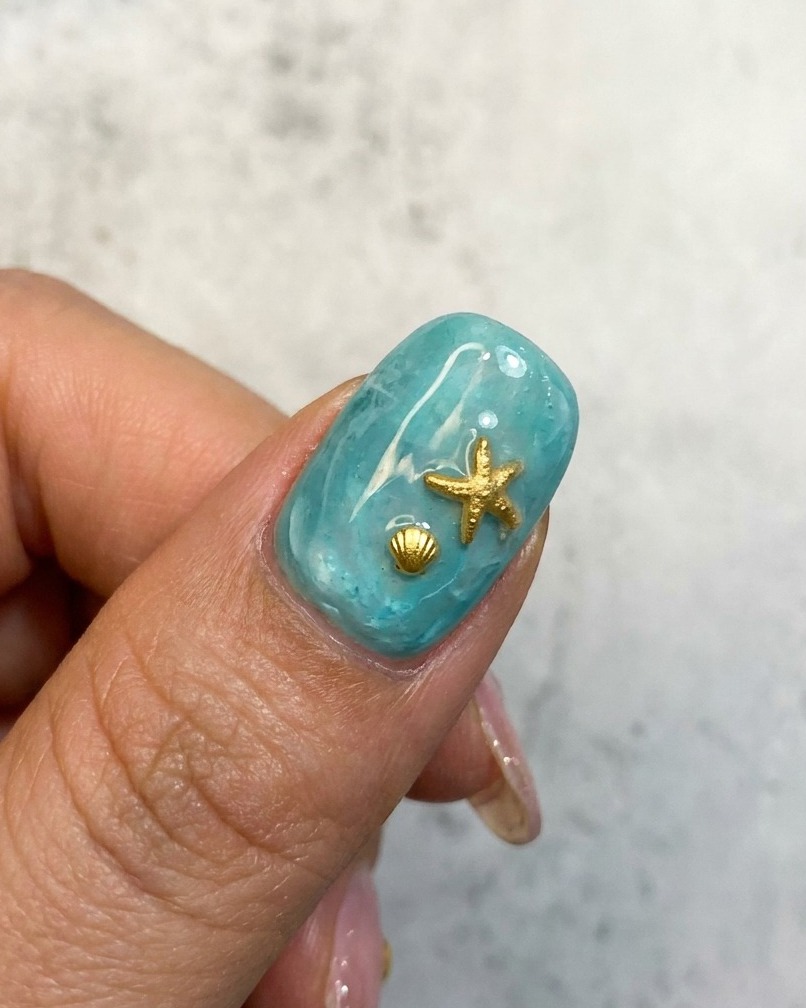 Eine Nahaufnahme eines blauen ozeanischen Nageldesigns mit einer goldenen Seestern- und Muschelverzierung.