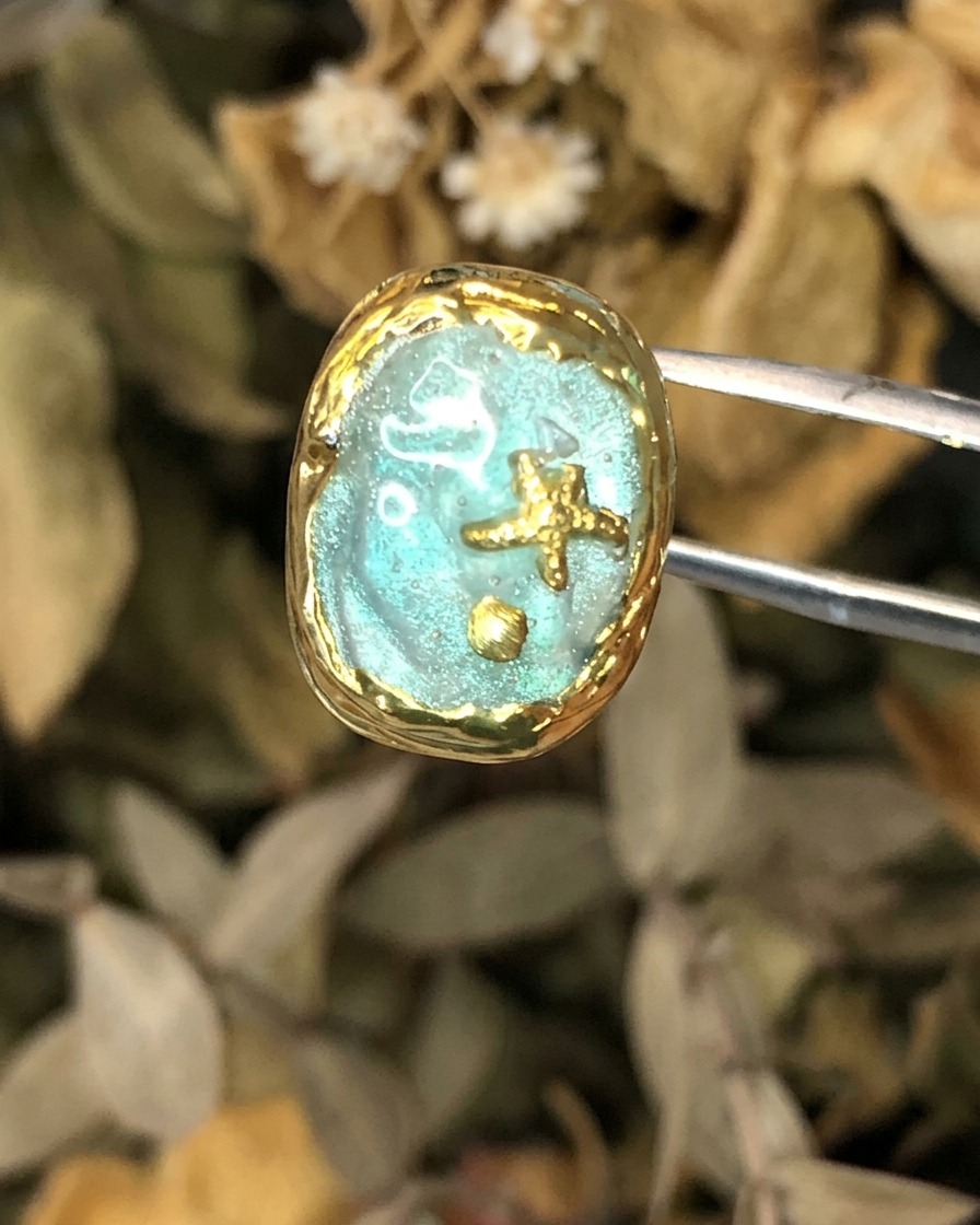 Eine Pinzette hält ein fertiges Nagelkunstwerk im Atlantis-Thema mit Goldrahmen.
