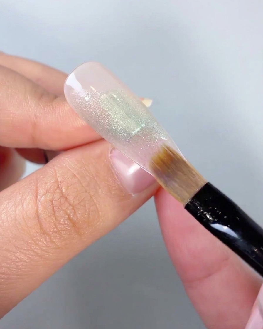 Eine Nahaufnahme eines weichen Pinsels, der die Kanten eines grünen Gel-Farbblocks auf einer Nagelspitze verblendet.