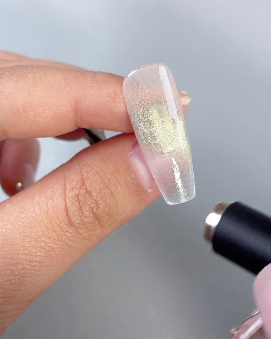 Ein zylindrischer Magnetstab, der nahe an ein glänzendes grünes Gelnagel gehalten wird, um den Cat-Eye-Effekt zu aktivieren.