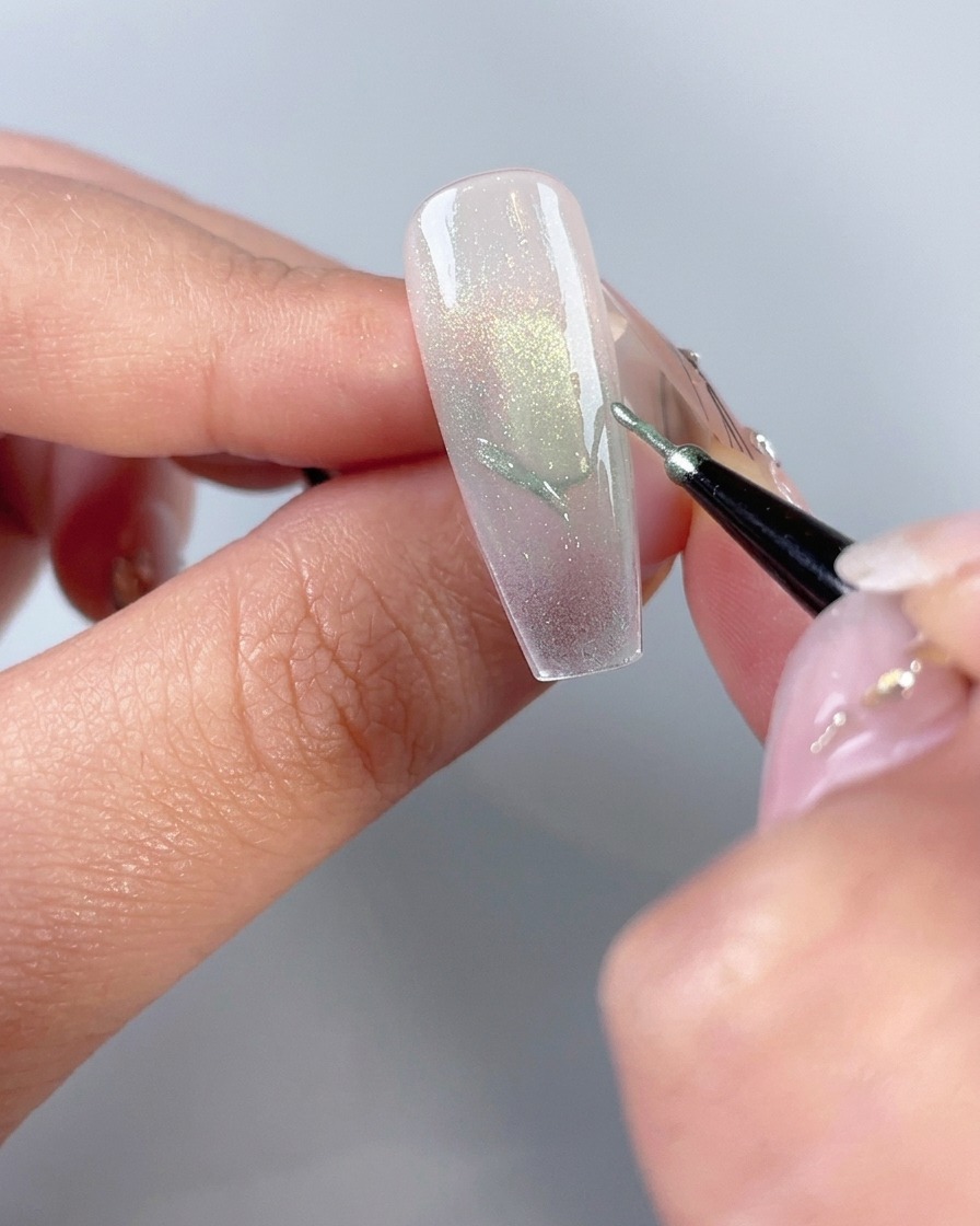Ein feiner Nail-Art-Pinsel zeichnet Schmetterlingsflügel-Umrisse auf eine manikürte Nagelspitze.
