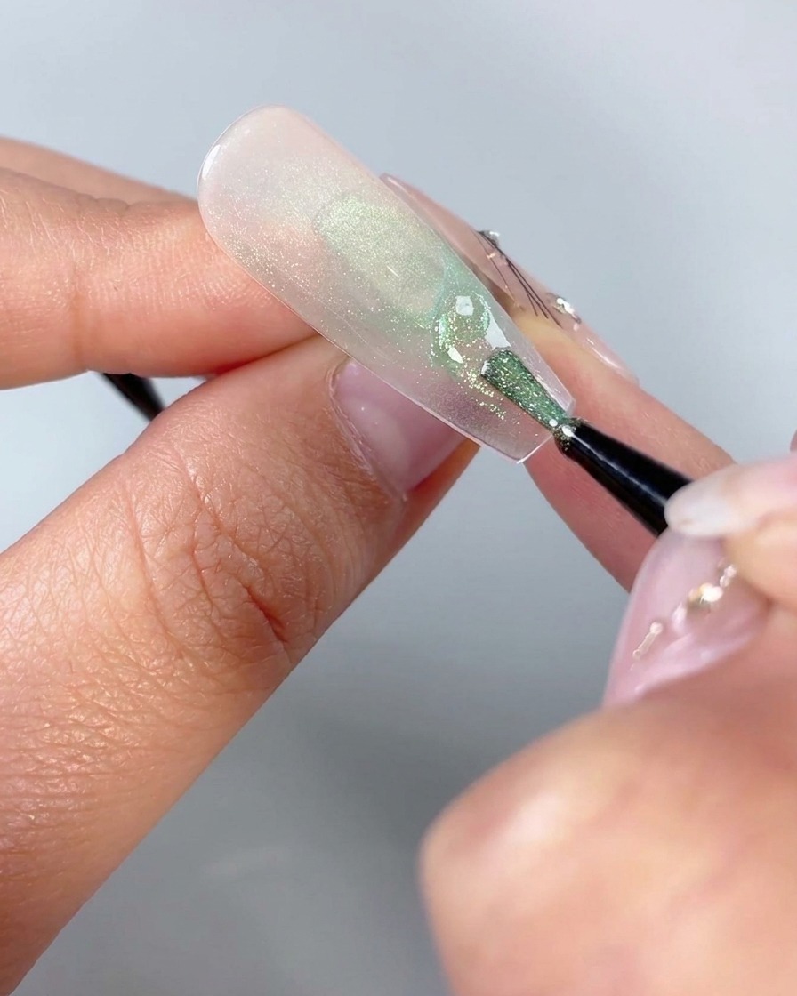 Ein feiner Nail-Art-Pinsel zeichnet kleine geschwungene Dreiecksformen nahe der unteren Basis eines Schmetterlingsnageldesigns.