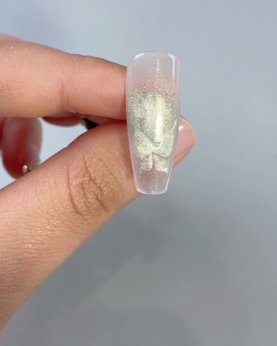 Eine Nahaufnahme einer klaren Nagelspitze, die leuchtende grüne Cat-Eye-Schmetterlingsflügelformen nach magnetischer Aktivierung anzeigt.