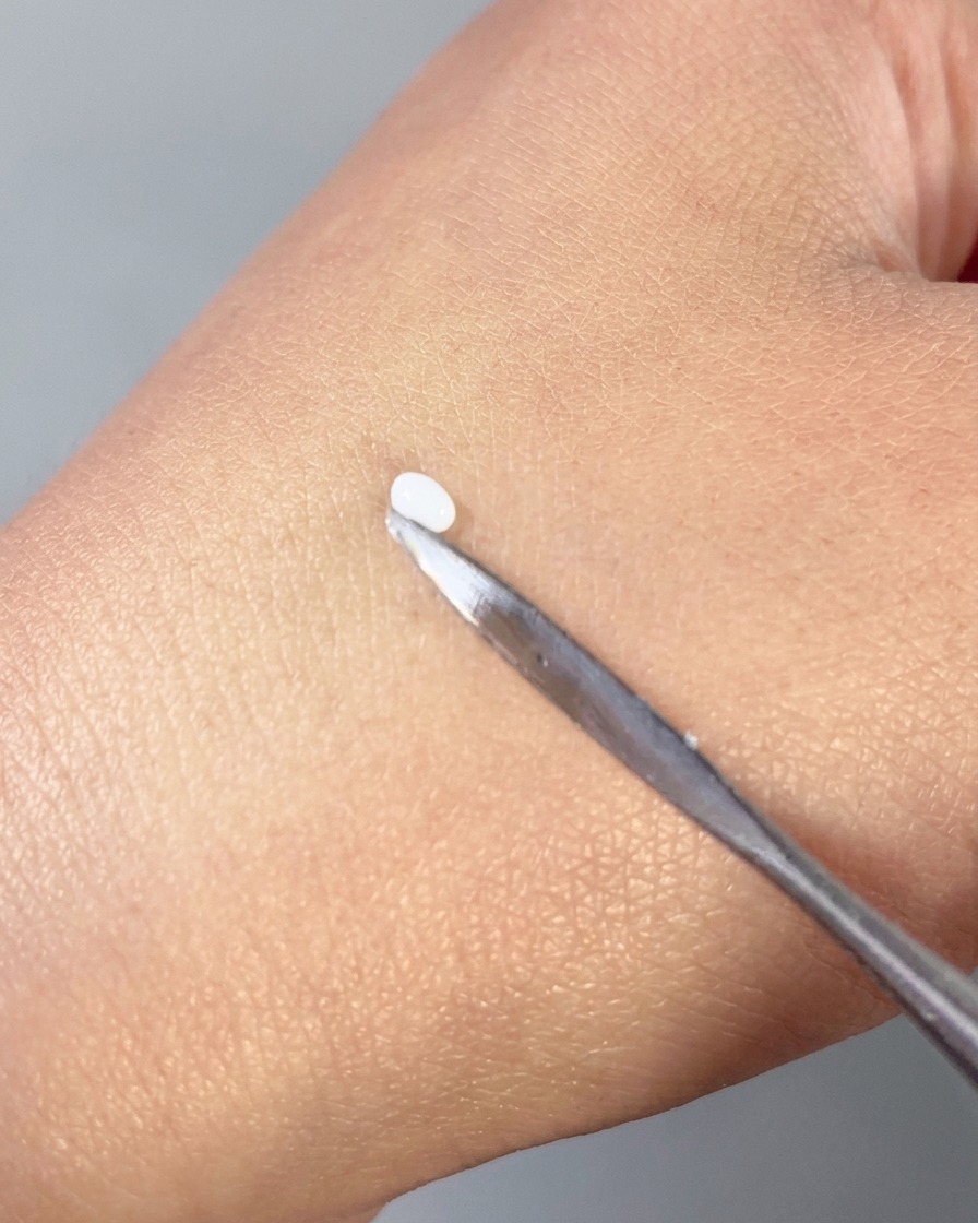 Ein Metallspatel drückt eine kleine weiße Perle aus 3D-Gel in eine glatte Blütenblattform auf dem Handrücken.