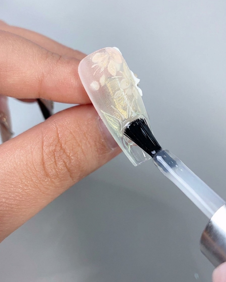 Ein Nagelpinsel trägt einen klaren Überzug auf die Unterseite der freien Kante eines klaren Verlängerungsnagels auf.