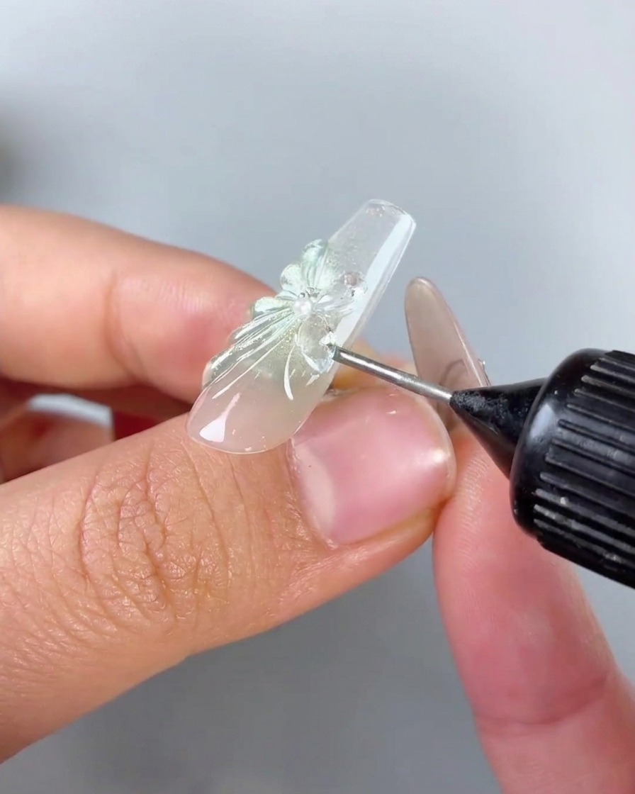 Eine Flasche mit Nadelspitze trägt klares Spaltfüllgel um die Basis und die Kanten eines Strass-Schmetterlings-Charms auf einem Nagel auf.