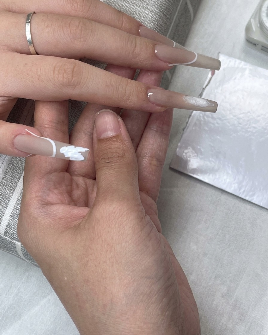 Ein French-Tip-Schablonenaufkleber ist auf dem Nagel platziert, während weißes Gel-Polish den Spitzenbereich ausfüllt.