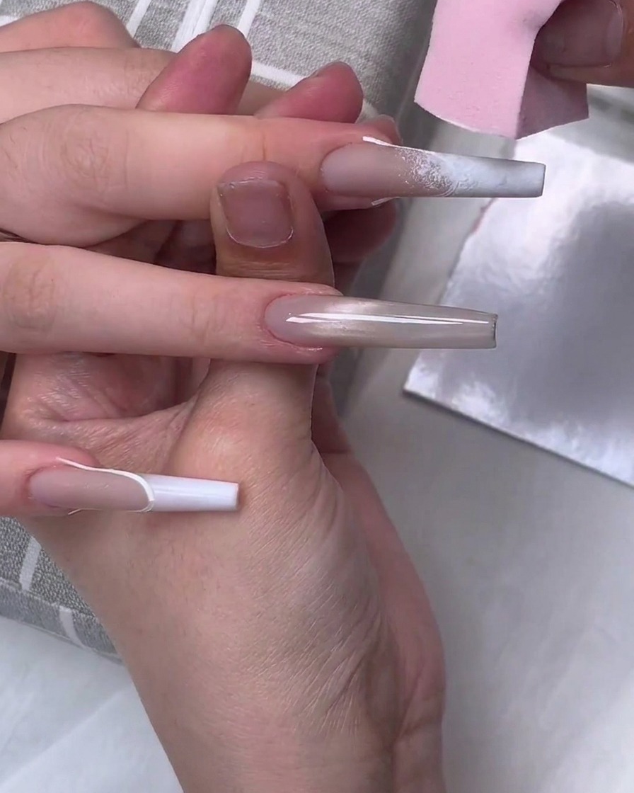 Ein rosa Make-up-Schwamm tupft weißes Gel-Polish auf die Spitze eines langen sargförmigen Nagels, um einen Verlaufseffekt zu erzeugen.