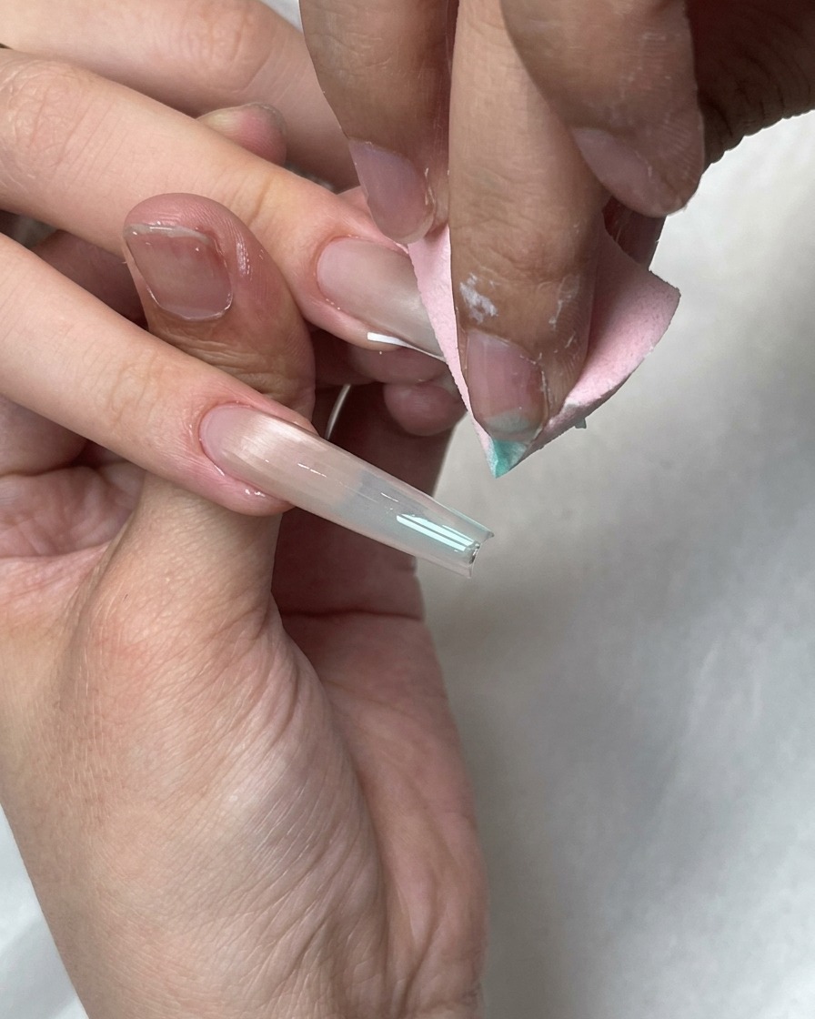 Ein rosa Make-up-Schwamm verblendet blaue Gelpunkte auf der weißen French-Spitze eines langen Nagels.