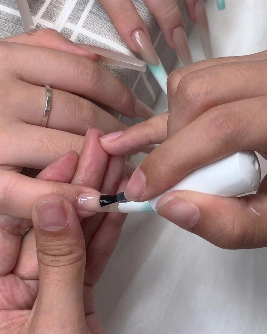 Ein Pinsel trägt klares Base- oder Top-Coat auf die Oberfläche eines verlängerten Nagels auf.