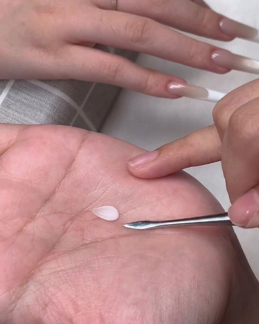 Ein kleines tropfenförmiges weißes 3D-Gelblütenblatt liegt auf der Handfläche einer Person neben einem Metall-Modellierwerkzeug.