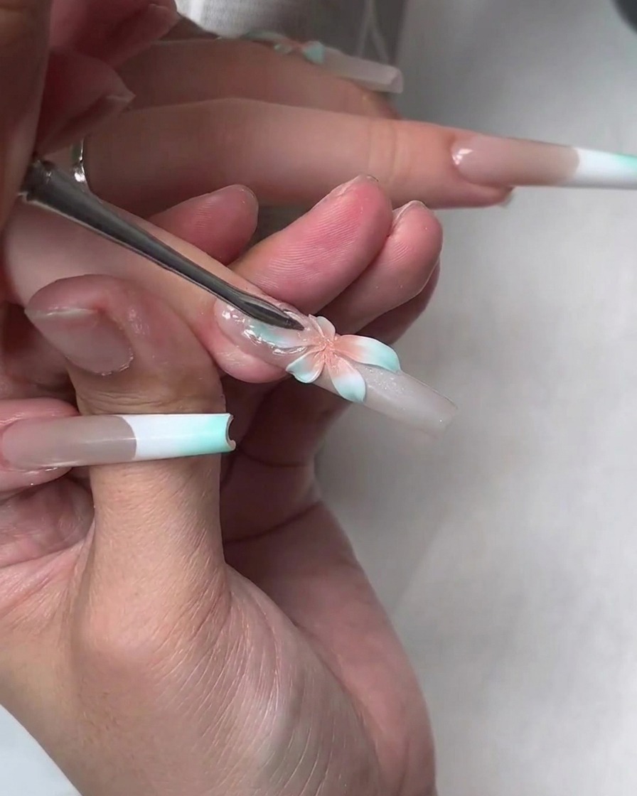 Ein Werkzeug drückt eine klare, weiche Builder-Gel-Schicht über die gemalte Blume, um größere transparente Blütenblätter zu erzeugen.