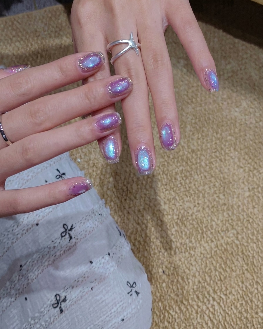 Ein Pinsel trägt eine Schicht schimmernden blau-lila Cat-Eye-Gel-Lacks auf einen Nagel auf.