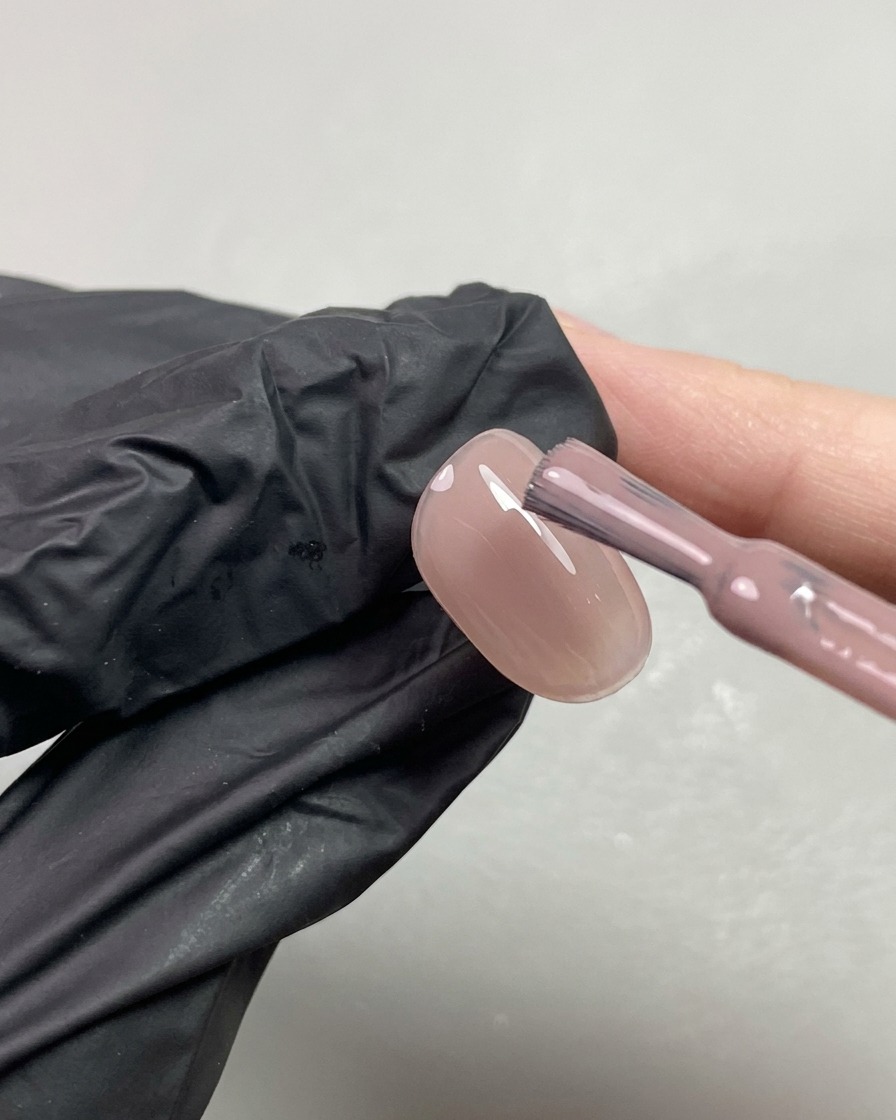 Ein Pinsel trägt eine zweite Schicht des nudefarbenen Gels auf einen Fingernagel auf.