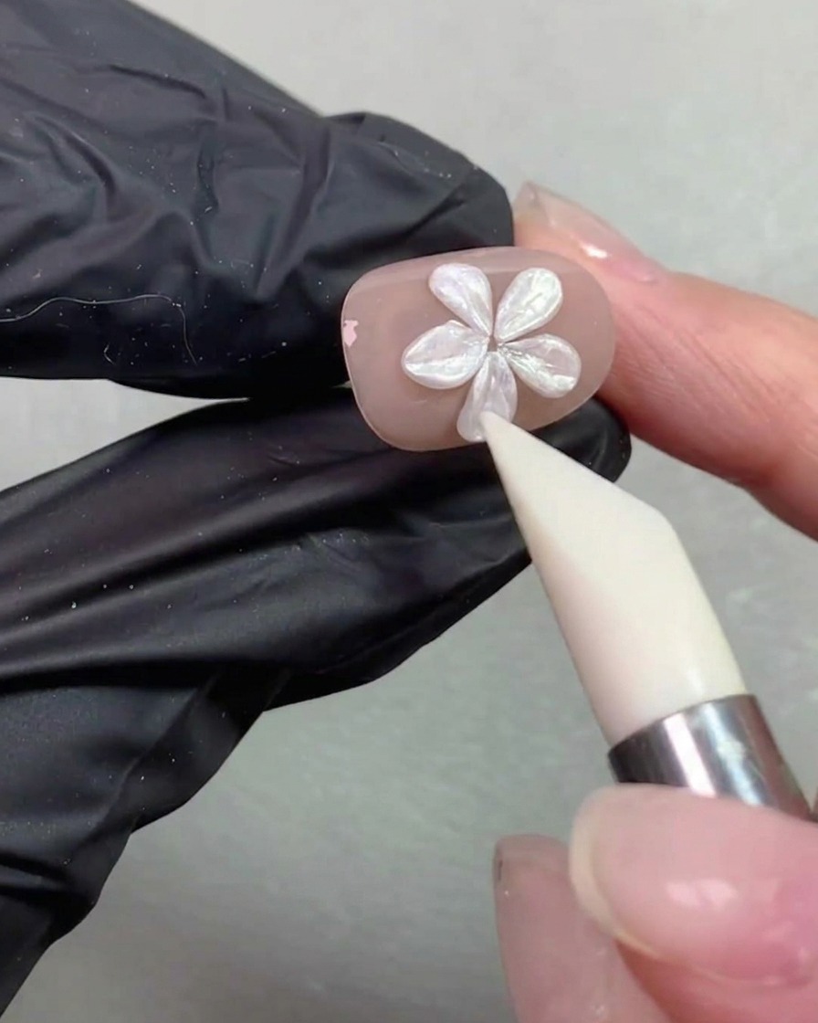 Ein Silikon-Formstift glättet und korrigiert die Konturen einer Perlenblume auf einem Nagel.