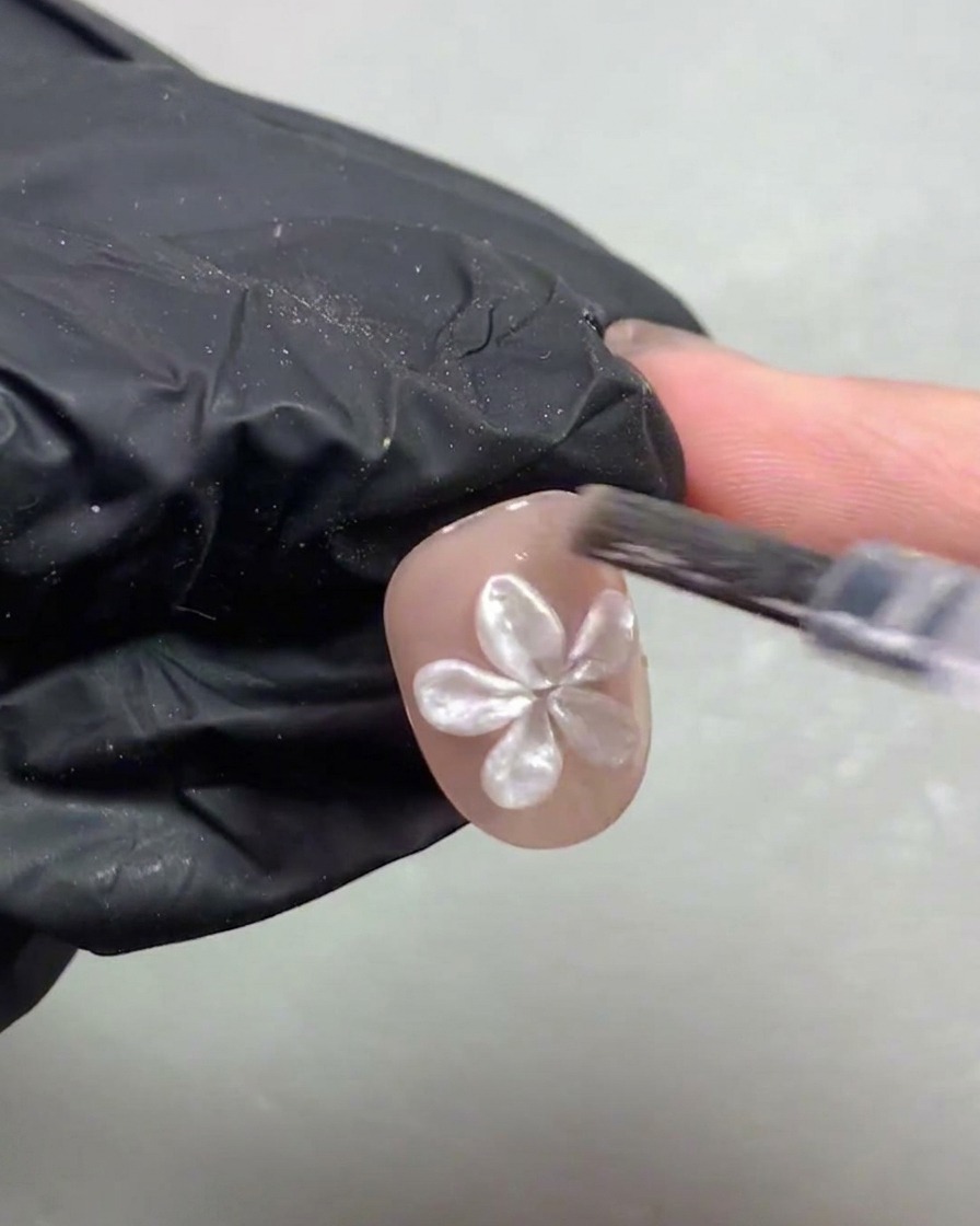 Eine Hand legt einen Nagel mit einer 3D-Perlenblume unter eine violette UV- und LED-Lampe.