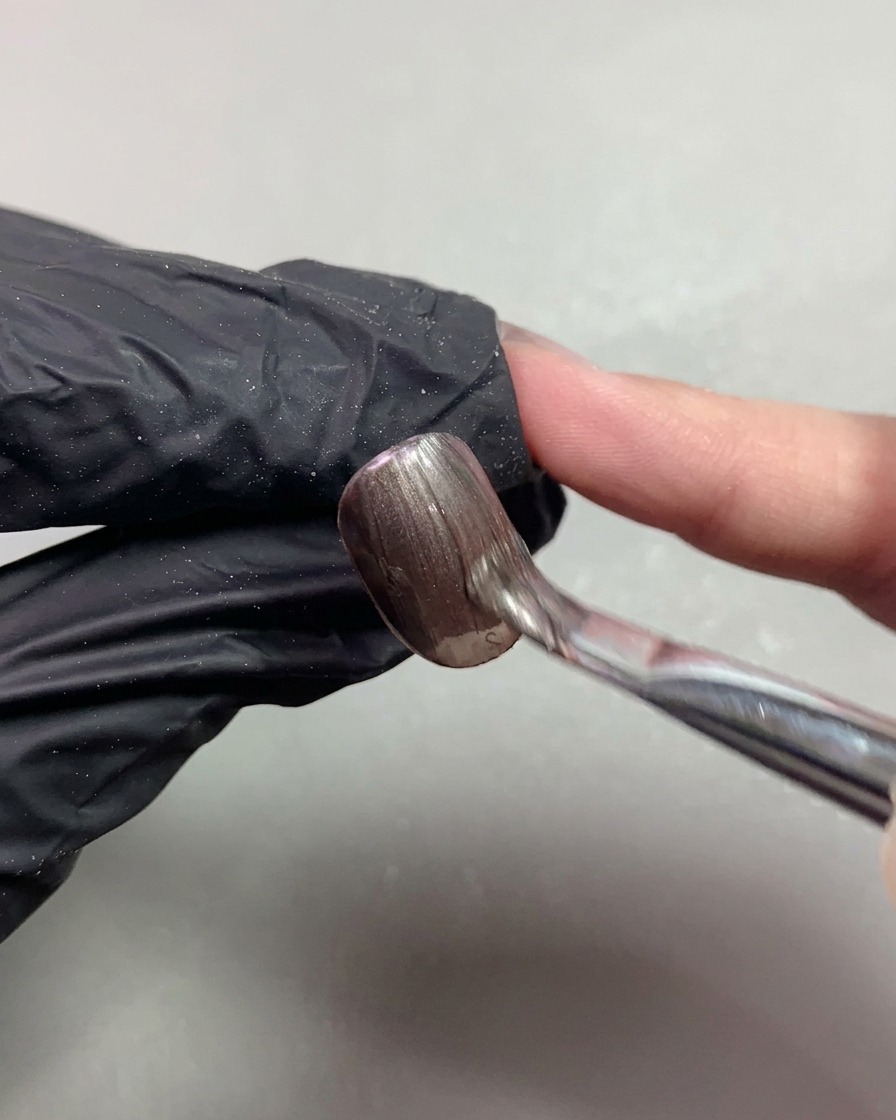 Ein Pinsel trägt dunkelbraunen magnetischen Cat-Eye-Lack auf einen kurzen Nagel auf.