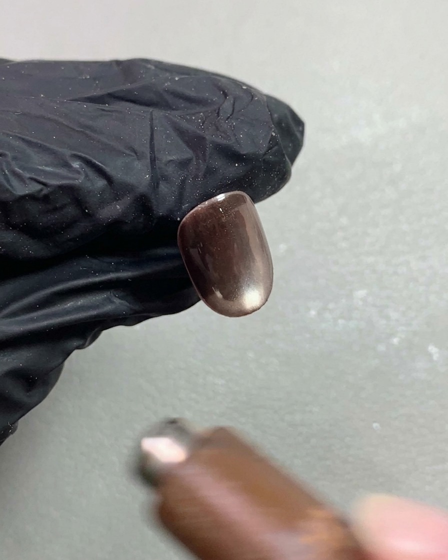 Ein Nagelmagnet schwebt über einem dunklen Cat-Eye-Nagel und formt einen hellen Lichtreflex.