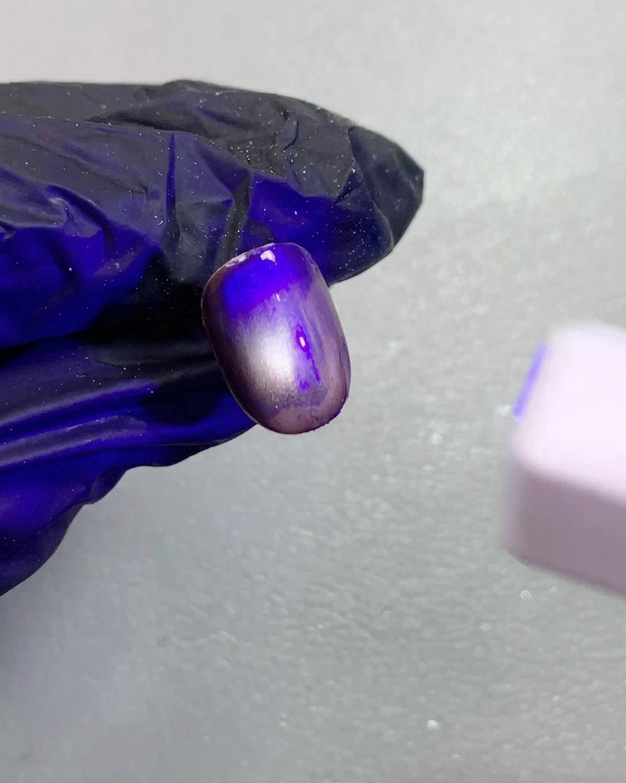 Eine Nahaufnahme des dunkelbraunen Cat-Eye-Nagels unter einer kleinen UV-Lampe.