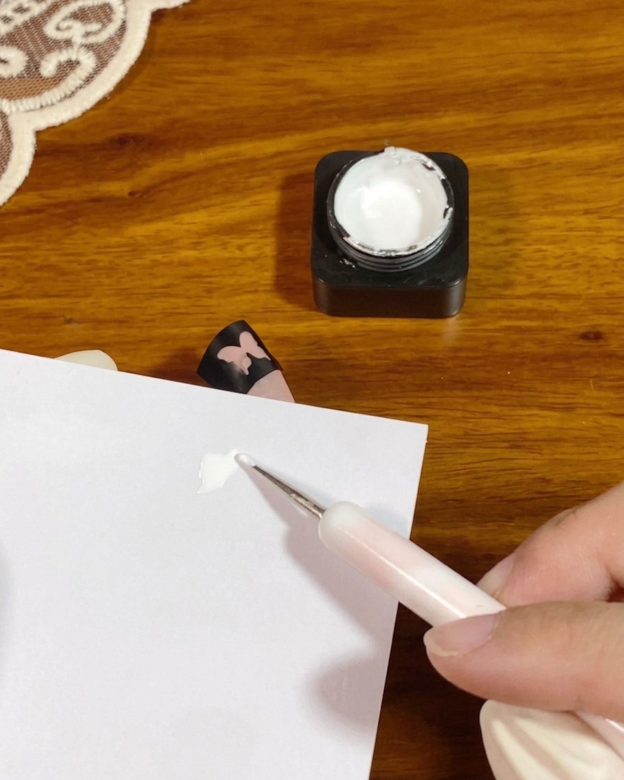 Ein Dotting-Tool gibt einen kleinen Klecks dickes weißes Tupfgel auf ein weißes Palettenpapier.