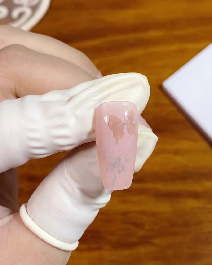 Eine Nahaufnahme einer behandschuhten Hand, die einen künstlichen Nagel mit einer Negativraum-Schmetterlingssilhouette hält.