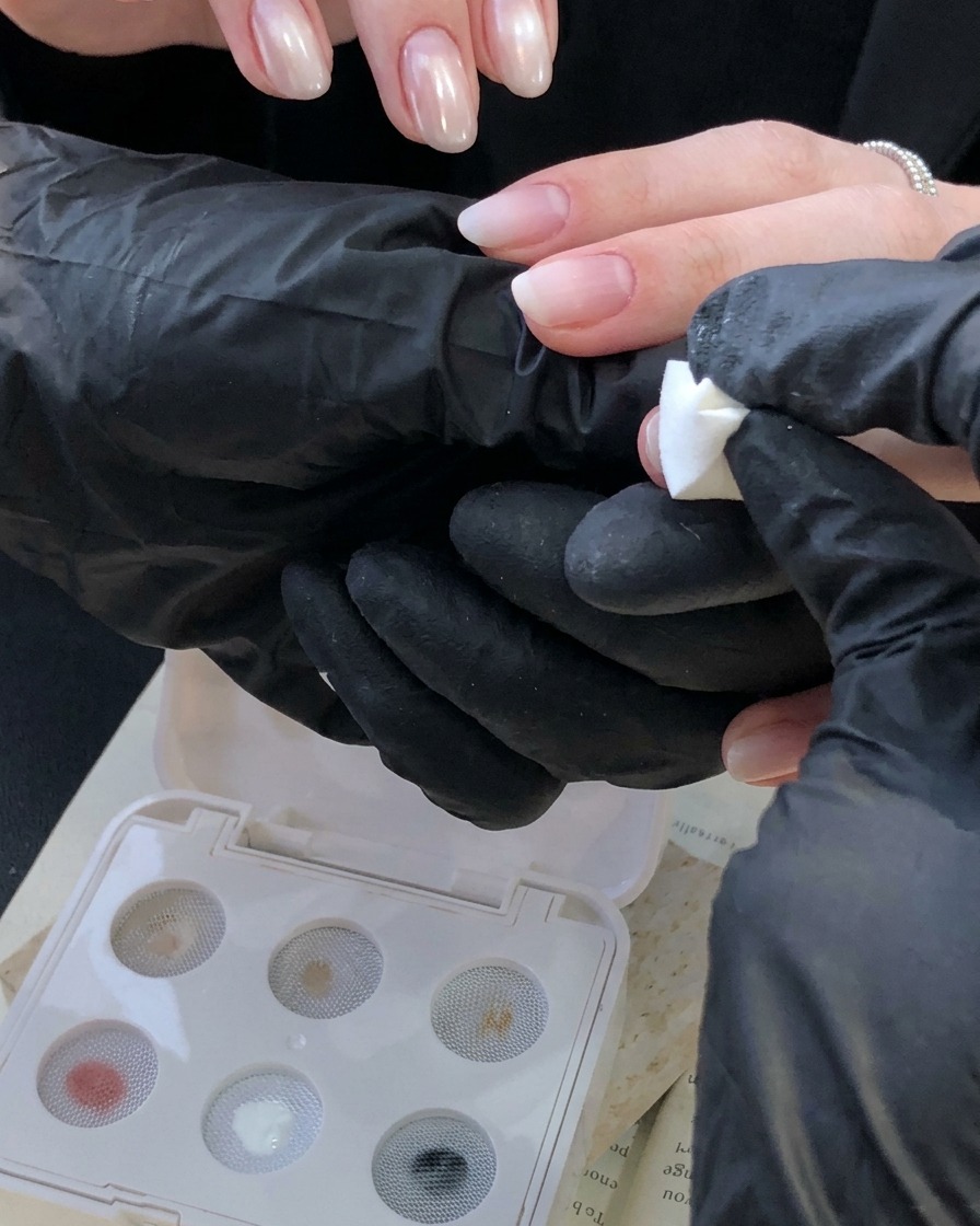 Eine bekleidete Hand, die einen weißen Schwamm-Stempel verwendet, um einen elfenbeinweißen Farbverlauf nahe der Nagelhaut auf einen Fingernagel aufzutragen.