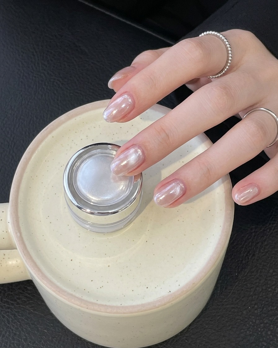 Eine Hand mit einem Ring hält einen kleinen silbernen Tiegel und präsentiert fertig glänzende Chromnägel.