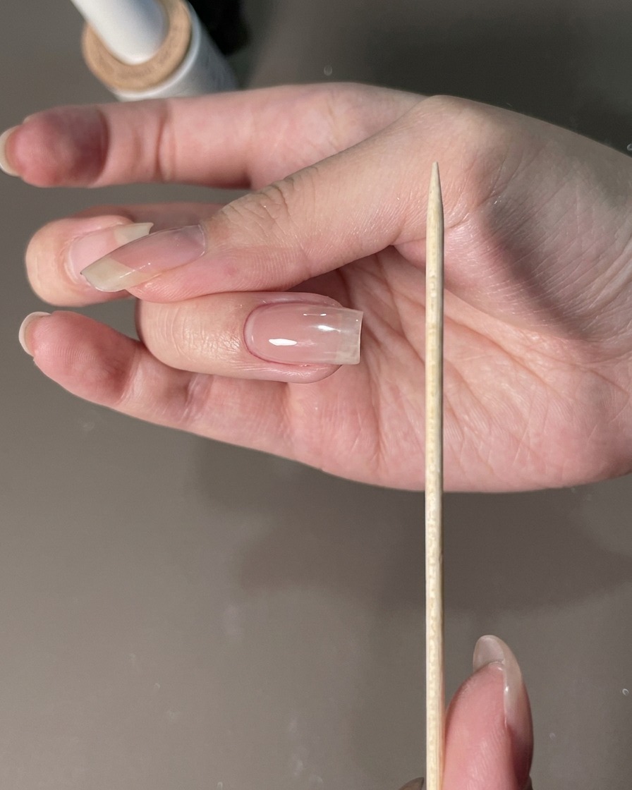 Eine Nagelfeile wird neben einer manikürten Hand gehalten, um die Nagelränder zu formen.